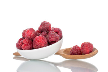 Several berries of ripe red raspberries on a white ceramic saucer with a wooden spoon, close-up, isolated on white.