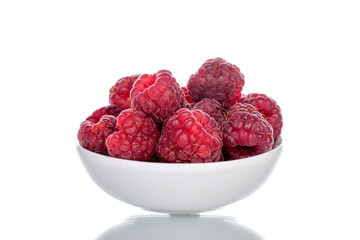Several berries of ripe red raspberries on a white ceramic saucer, close-up, isolated on white.