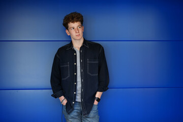 Portrait of young man standing against blue background outdoors.