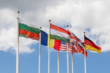 Several flags of various countries of the world flutter in the wind, against a cloudy sky. Flags of different states together - as a symbol of world cooperation. Various flags on flagpoles