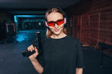 Confident female shooter in safety goggles looking ahead - obrazy, fototapety, plakaty