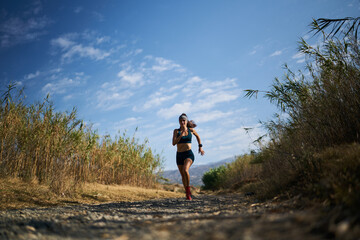 pretty young female athlete running on a dry river bed with hot summer temperatures