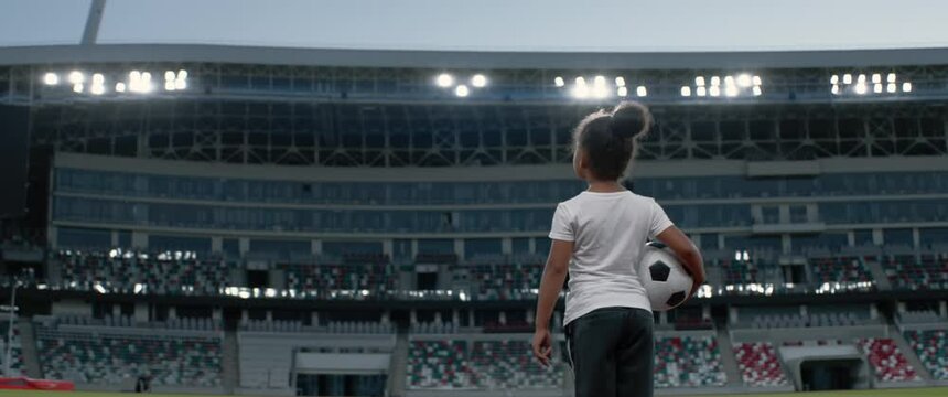 Portrait of African American Black dreamer child girl walking onto the field of huge soccer football stadium, holding a ball, dreaming of becoming professional player, soccer star. Women sport concept