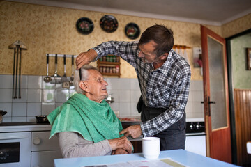 Fototapeta premium Portrait of man combing hair of elderly father indoors at home.