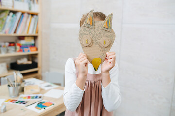Little girl holdng cardboard handmade fox mask over her face. At a child learning center.