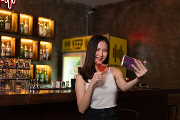 Nightlife concept a sexy girl with smiling face doing selfie on her smartphone while hold a vivid...