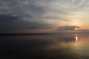 Obraz premium Sunbeam from clouds at sunset over calm lake water