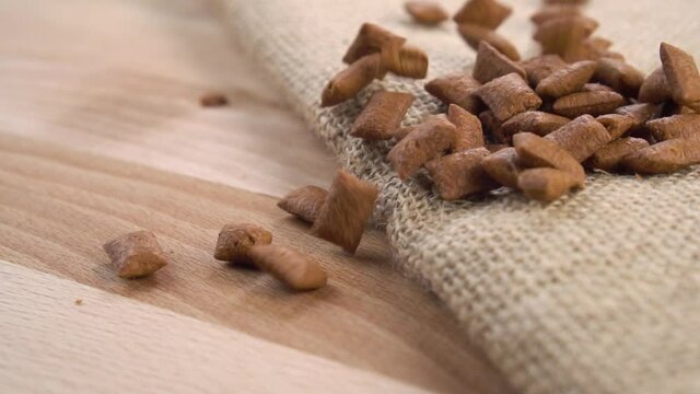 A dry pet food snack treat falls on a sackcloth on a wooden surface. Macro. Slow motion
