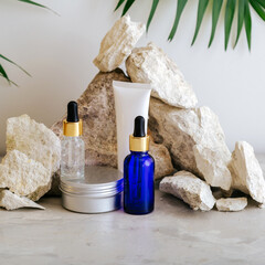 Set natural beauty cosmetic skincare products with palm leaf plant on stone pedestal, rock pile balancing stones gray background. Serum cream butter body care cosmetic mockup. Minimalistic square