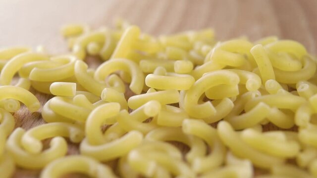 Falling dry uncooked italian gobbetti pasta on a wooden table in slow motion. Macro. Traditional Italian Mediterranean cuisine. Raw macaroni