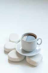 A white cup of coffee on white table, decorated with white stones. Still life for interior design.