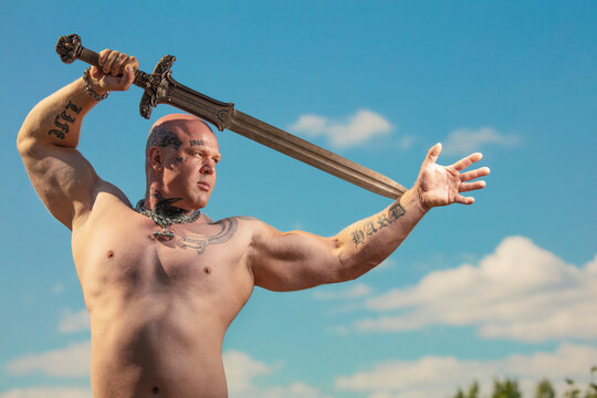 Espoo, Finland, 25 July 2021. A man with tattoos, athletic, bodybuilding, with a naked torso, with a fighting sword in the background of nature.