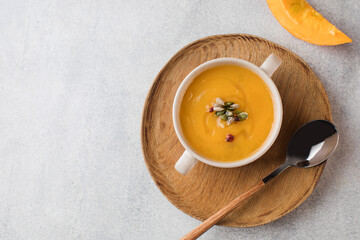 Pumpkin cream soup in a bowl with seeds on a gray background. Comfortable riding, autumn menu. Copy space,