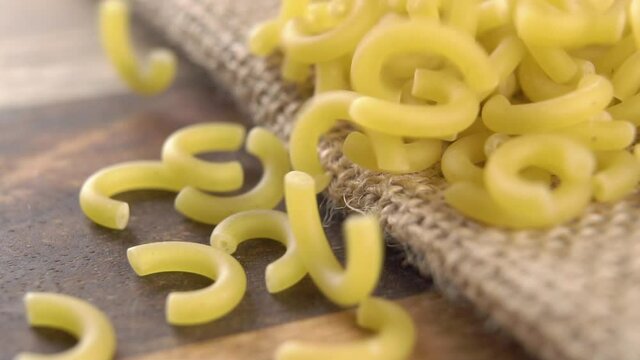 Uncooked Italian gobbetti pasta falls on rustic rough burlap and wood. Macro. Dry macaroni. Slow motion. Mediterranean cuisine concept