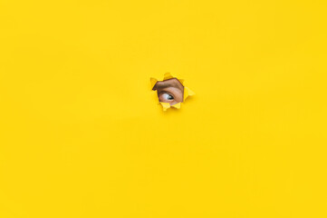Left eye looking through a hole in a yellow paper. Voyeurism. The man is watching the wife. A curious look. Jealousy, spying on or overhearing the concept. Copy space.