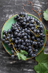Black grapes in plate with vine plant on dark table top view. Sweet juicy grapes food on black concrete background flat lay Vertical