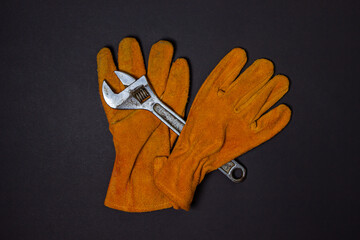 Construction yellow gloves and an adjustable wrench on a black background. Workshop and male work concept.