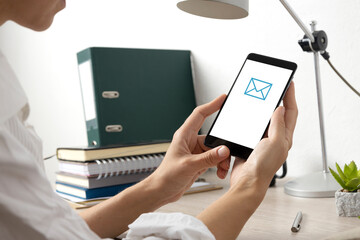 Woman holding smartphone, get message and reading it.Office desk and lamp,notebooks on it.Empty space