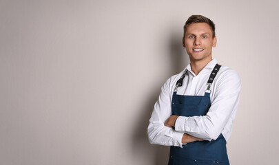 Portrait of happy young waiter in uniform on light background