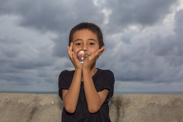 .A boy holding a crystal ball beside wave barrier at Kata beach Phuket Thailand..cloud above island...