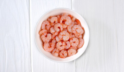 Boiled shrimps in a white plate on a wooden table. Seafood copy space.