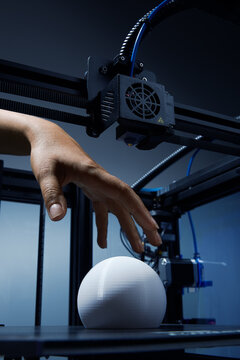 A gender-neutral hand reaching out 3d printed round white object made from recycled plastic to pick up. Futuristic concept of new working possibilities for small businesses by 3D printing. Jpg photo