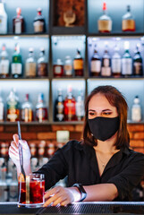 Portrait of young attractive woman bartender with mask Making Cocktail in bar