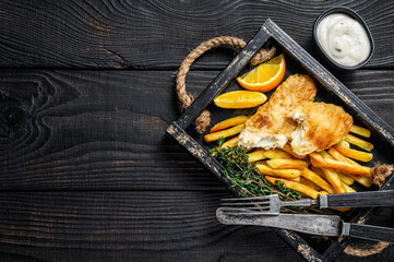 Battered Fish and chips dish with french fries and tartar sauce in a wooden tray. Black wooden...