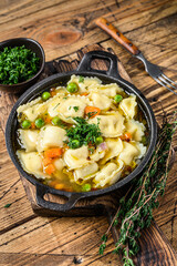 Broth soup with ravioli dumplings pasta in a pan. Wooden background. Top view