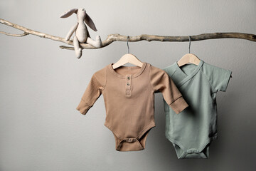 Baby bodysuits and toy on decorative branch near light wall