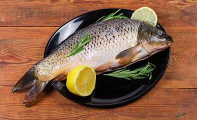 Raw carp prepared for cooking, rosemary, lemon on black dish