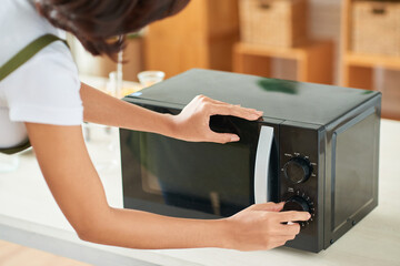 Young woman setting time on microwave when drying orange and lemon slices in for making organic...