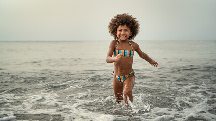Afro child having fun playing inside sea water during summer holidays - Childhood and travel vacation concept
