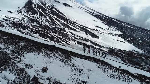 A group of mountaineers-tourists is walking on a half-snow-covered rock. Beautiful and exciting shooting from the air.
