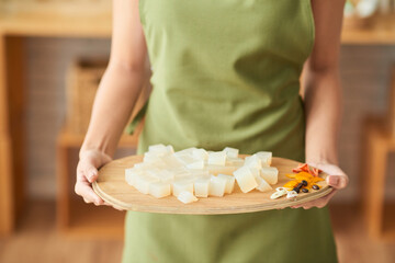 Woman holding wooden tray with ingredients for making organic soap