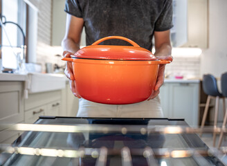 A man holding in his hands orange enamel dutch oven.