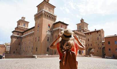Travel in Italy. Back view of beautiful tourist girl enjoying view of Este Castle (Castello Estense) of Ferrara, Italy. - obrazy, fototapety, plakaty
