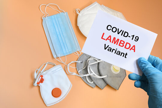 Doctor's hand in blue glove with white paper and text Covid-19 Lambda + Variant with various protection masks on background. COVID-19 lambda variant strain protection concept.