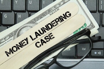 laptop keyboard, glasses, paper money, ice cream stick with the word money laundering case
