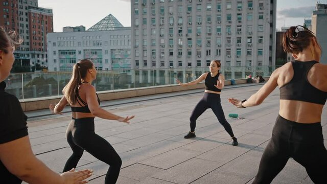 Diversity group of women, of different ages, builds and looks, have a sport dance class. Women dancing zumba in the city square together with a young female trainer