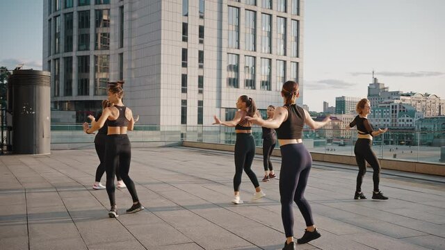Young women dancing zumba on the city background. A group of girls is practicing outdoor sports dances, like-minded women are training on the street