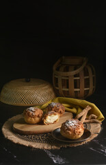 luxury home made chilled vanilla cream puff pastry choux with sugar powder on wood plate and cloth in black background and bamboo basket prop dessert halal menu