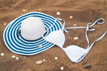 white women's swimsuit lies on the sand with seashells along with a sun hat.