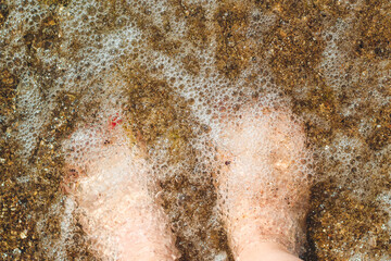 female legs on the beach in sea foam.