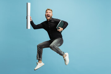 Funny portrait of young bearded man, builder, designer or architect with professional equipment jumping isolated on white studio background.