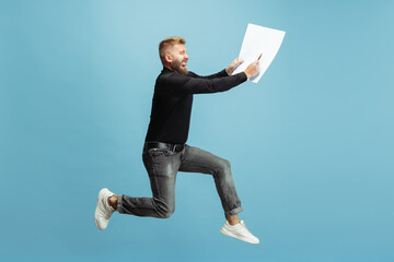 Funny portrait of young bearded man, builder, designer or architect with professional equipment jumping isolated on white studio background.