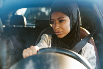 Black muslim woman wearing headscarf looking aside while driving car