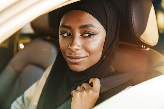 Black woman wearing headscarf smiling while driving car