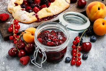 Jar of cherry jam among fresh fruits on wooden table.