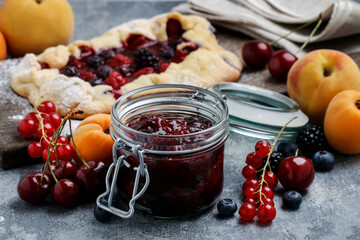 Jar of cherry jam among fresh fruits on wooden table.